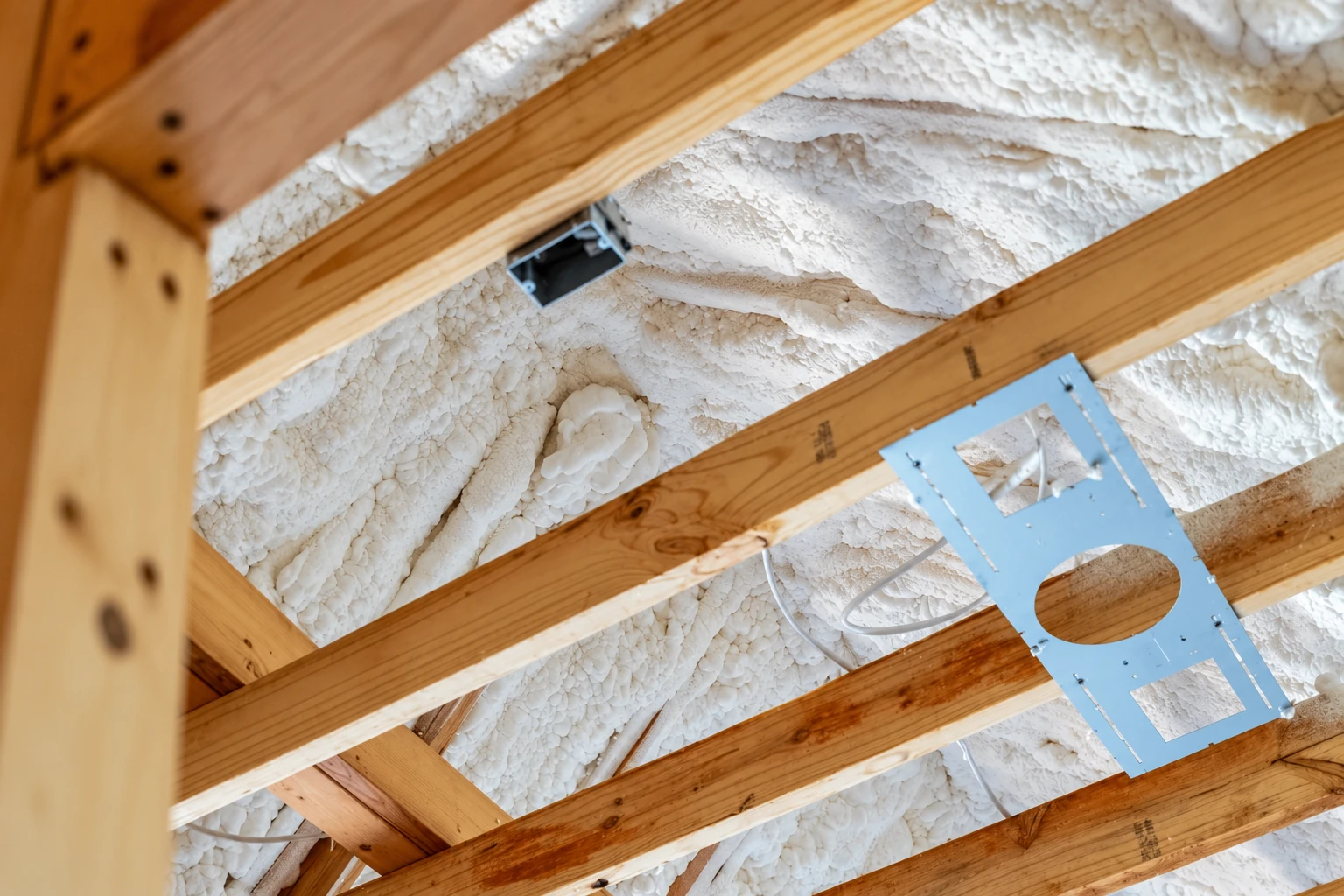 White spray foam coats the underside of a roof between exposed wooden rafters.